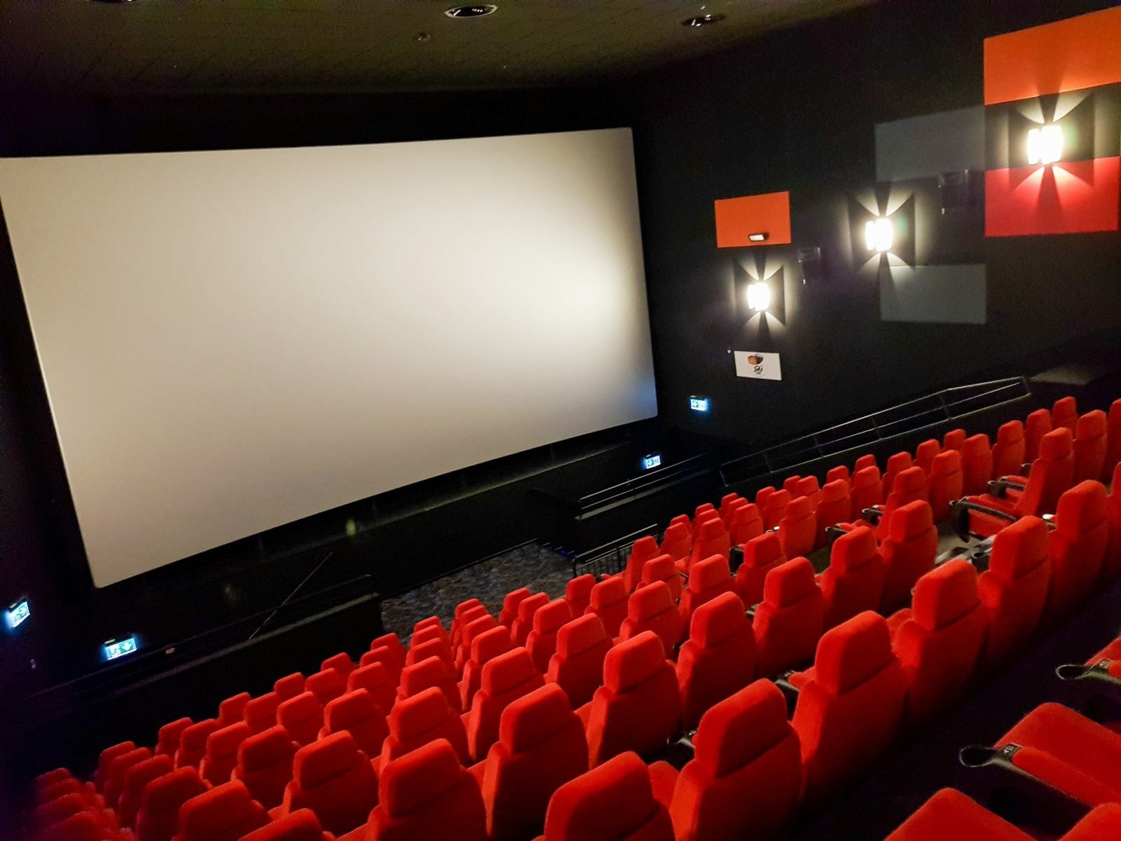 Empty red-seated movie theater auditorium with a large blank screen, illustrative photo