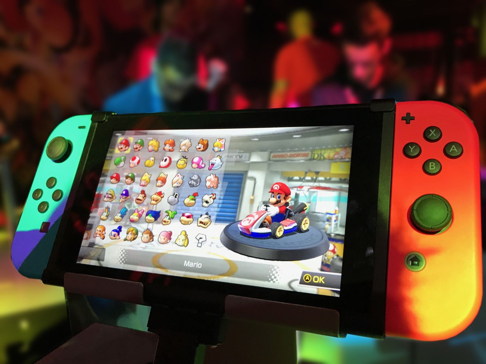 Nintendo Switch console on a stand showing a character select screen with colorful lights in the background, illustrative photo
