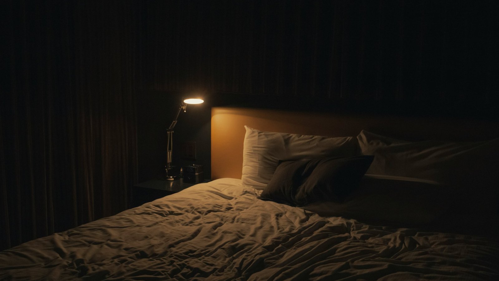A dimly lit bedroom with a rumpled bed and a single lamp glowing, an illustrative real photo for Jessica Chastain's horror film Other Mommy