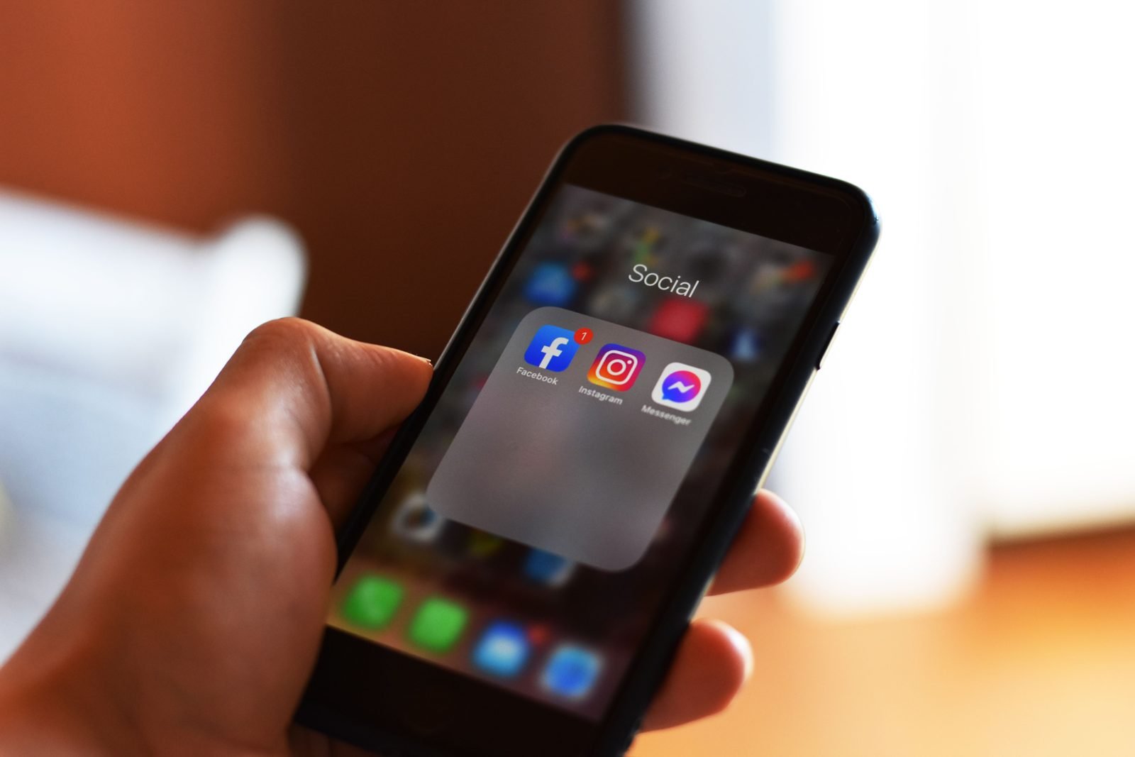 Hand holding a smartphone showing the Facebook, Instagram and Messenger apps in a Social folder, illustrating The Social Reckoning, the film about the Facebook whistleblower and Meta