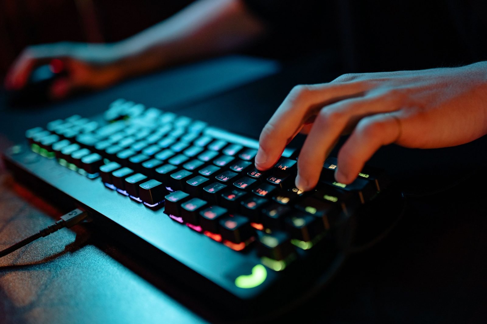 Hand typing on a backlit RGB mechanical gaming keyboard in a dark room, illustrative photo